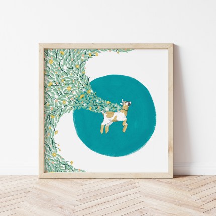 Shows a drawing of a happy pygmy goat with a cape of green leaves and buttercups against a turquoise circular background. The drawing is framed in a pale wood square frame, which rests on a pale herringbone floor against a white wall.
