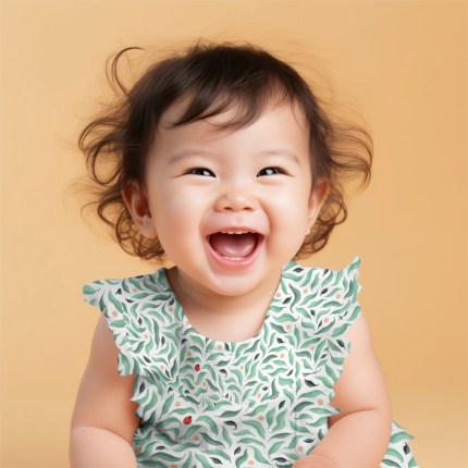 A little girl (around 18 months old) smiles into the camera with a great big smile. She wears a frilly dress featuring a seamless pattern by Howell Illustration. The pattern features green leaves with tiny hidden ladybirds. The girl is set against an orange background.
